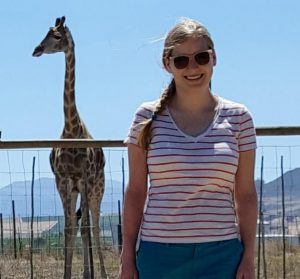 Picture of computer science student Carissa Bleker, standing outside with a giraffe standing behind her.
