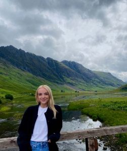Engineering in London student Madi Thomas standing near a lake with mountains in the background