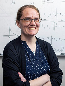 Assistant Professor Catherine Schuman stands in front of a white board with mathematical formulas written on it.